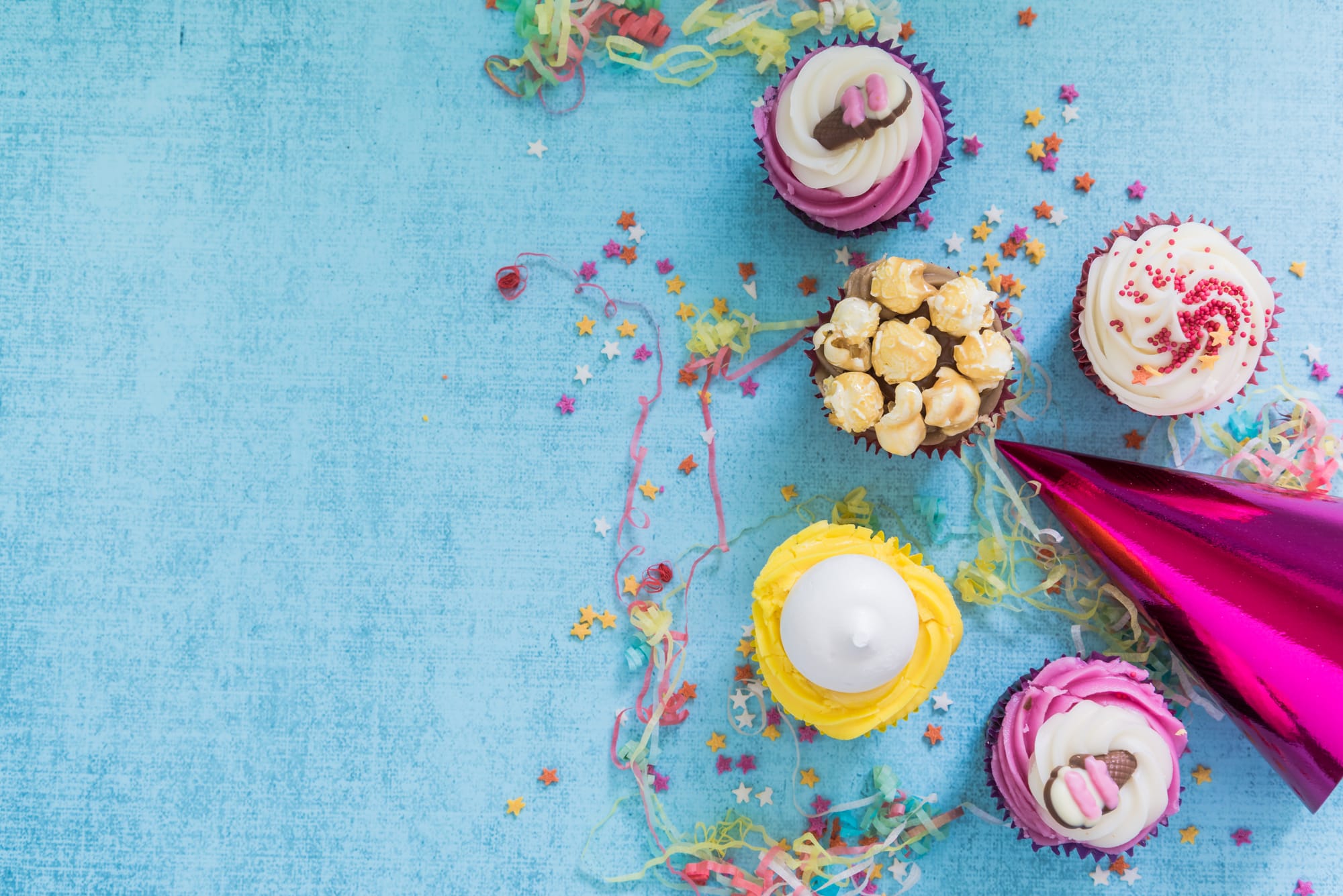 Blue background with party hat, confetti and cupcakes